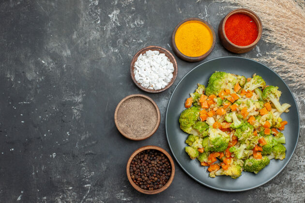 新鲜健康餐 黑盘子上放花椰菜和胡萝卜 灰色桌子上放香料健康一餐午餐香料