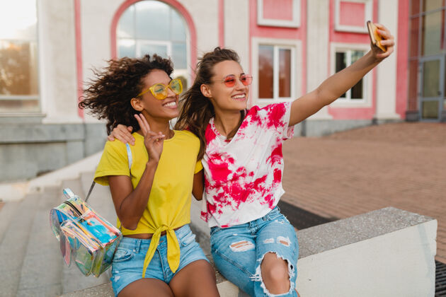 非裔美国人五颜六色的照片 快乐的年轻女孩朋友们微笑着坐在街上用手机自拍 女人们在一起玩得很开心欢呼眼镜兴奋