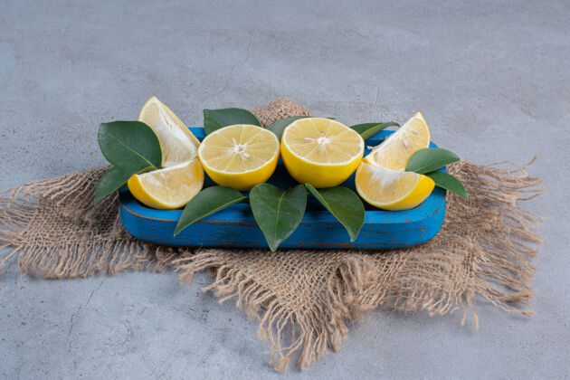 水果多汁的柠檬片和叶子放在大理石背景的蓝色盘子里拼盘美味美味