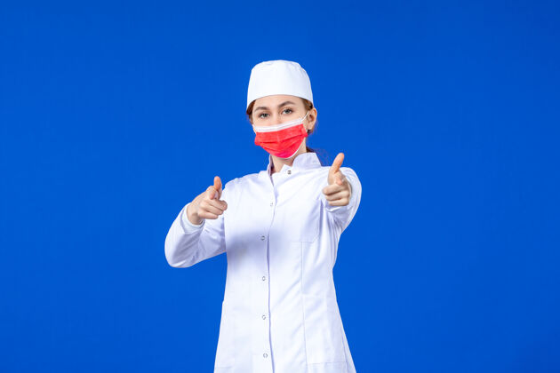 人正面图身着医疗服的年轻护士 蓝色墙上戴着红色防护面具工作防护正面