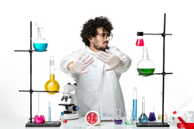 办公桌正面图身着特殊套装的年轻男性科学家站在桌子旁 白色桌子上摆着解决方案实验室烧杯套装
