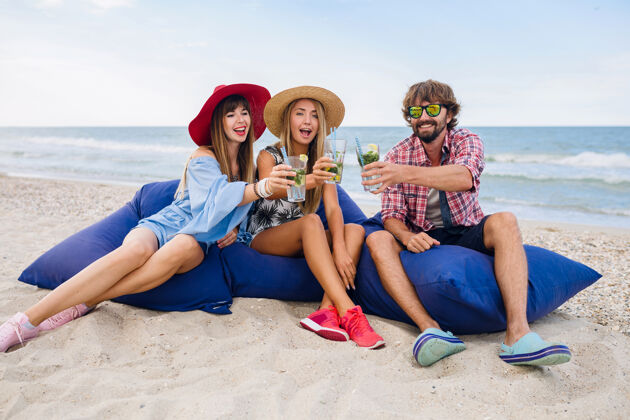 鸡尾酒年轻的微笑着度假的朋友们坐在豆包里参加沙滩派对聚会欢呼微笑