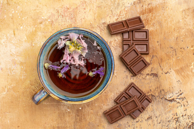 旧的上图：一杯热花草茶和巧克力棒放在五颜六色的桌子上杯子混合凉茶