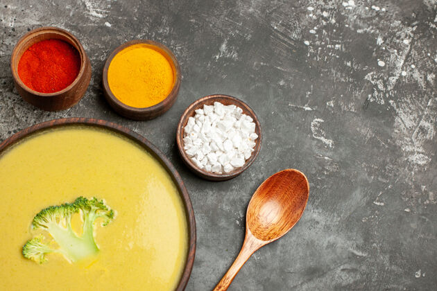 餐具棕色碗中的奶油西兰花汤和灰色桌子上的不同香料的水平视图食物午餐餐厅