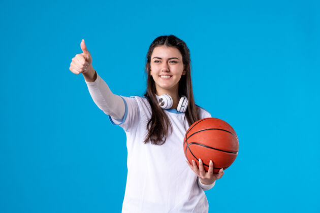 成人正面图：蓝色墙上挂着篮球的年轻女子女人竖起大拇指