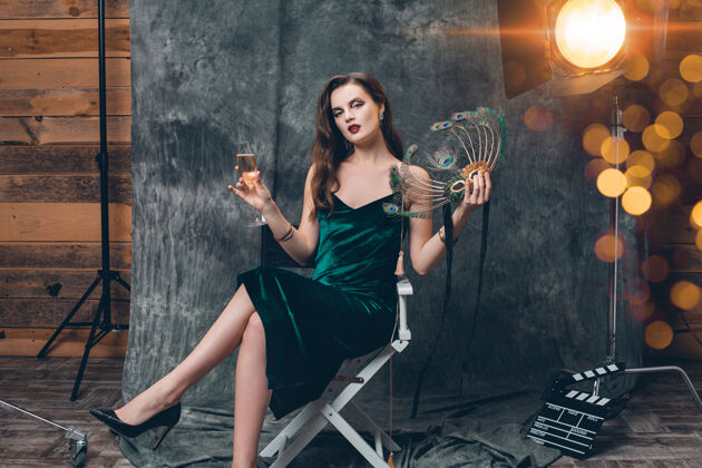 女人年轻时尚性感的女人坐在电影院后台的椅子上 用一杯香槟庆祝灯光魅力名人
