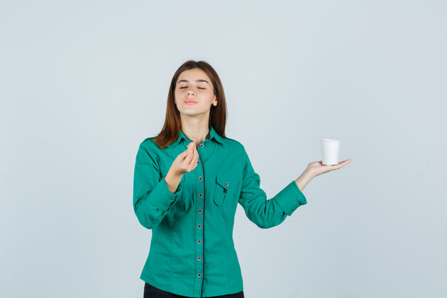 杯子年轻的女士手里拿着一杯塑料咖啡 一边在衬衫上摆出美味的姿势 神情愉悦 俯瞰前方微笑时尚咖啡