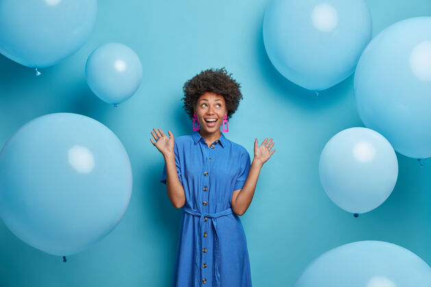 专注积极无忧无虑的非裔美国妇女准备庆祝 穿着节日服装 对着蓝色气球摆姿势华丽庆祝非洲