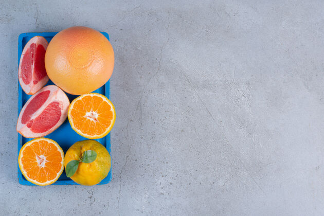 天然把整个橘子和葡萄柚片放在一个蓝色的小托盘上 放在大理石背景上切片美味健康