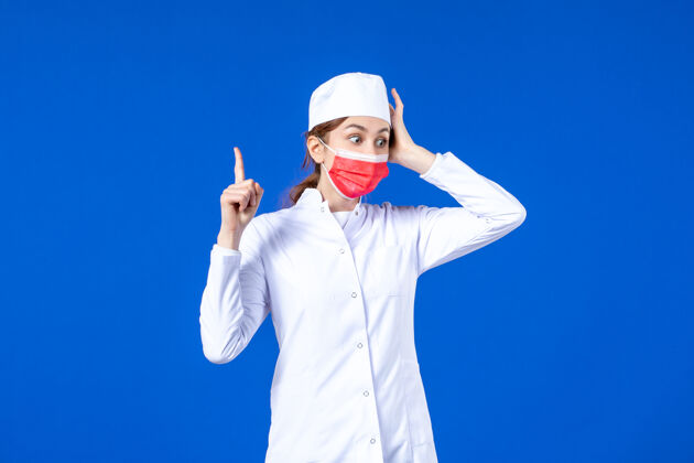 面罩正面图身着医疗服的年轻护士 蓝色墙上戴着红色防护面具防护人正面