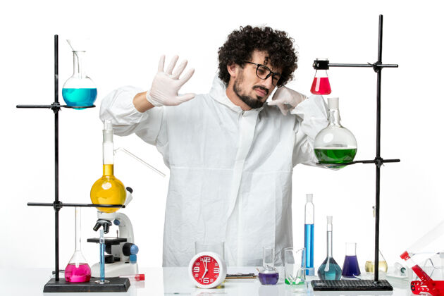 化学正面图身穿白色特殊套装的年轻男性科学家站在桌子旁 拿着解决方案研究周围科学