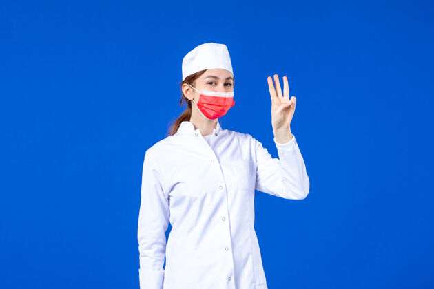 成人正面图身着医疗服的年轻护士 蓝色墙上戴着红色防护面具疾病蓝色面具