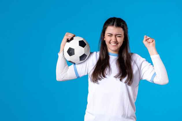 足球前视图：年轻女子在蓝色墙上拿着足球举行游戏体育