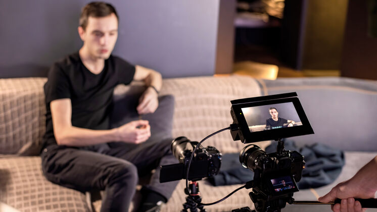 男人三脚架上的两个专业摄像机拍摄了一个坐在家里沙发上会说话的男人在家工作互联网剪辑男性