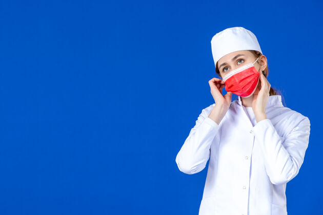 流行病身穿医疗服的年轻护士的正视图 蓝色的面具上有红色的面具医院疾病年轻护士
