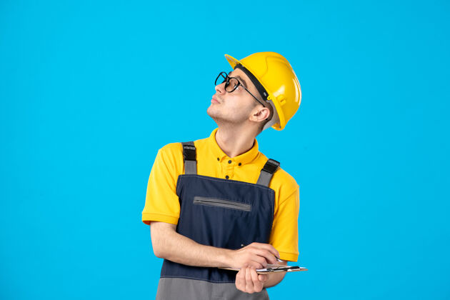 笔记穿着黄色制服的男工人的正面图 蓝色上有文件记录建筑杂务工工作