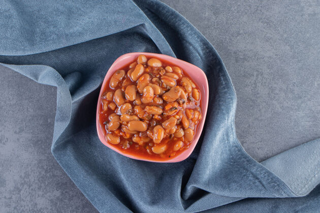美味在一块布上的碗里烤豆子 在蓝色的表面上烘焙自制美味