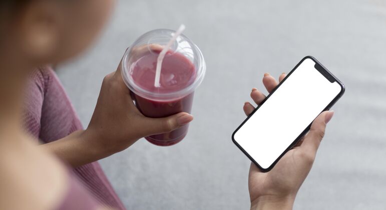 自然女性手里拿着果汁和智能手机 屏幕一片空白移动应用程序健身热带