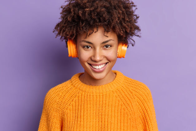 快乐快乐女音乐爱好者戴着无线立体声耳机的特写镜头欣赏播放列表中最喜爱的歌曲种族非洲毛衣