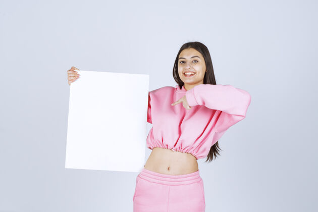 模型穿着粉色睡衣的女孩拿着一块空白的正方形展示板 指着它晋升成人人类