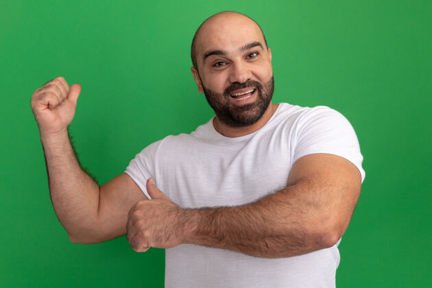 站着一个留着胡子的男人穿着白色t恤 快乐地用手指指着绿色的墙男人手指胡子