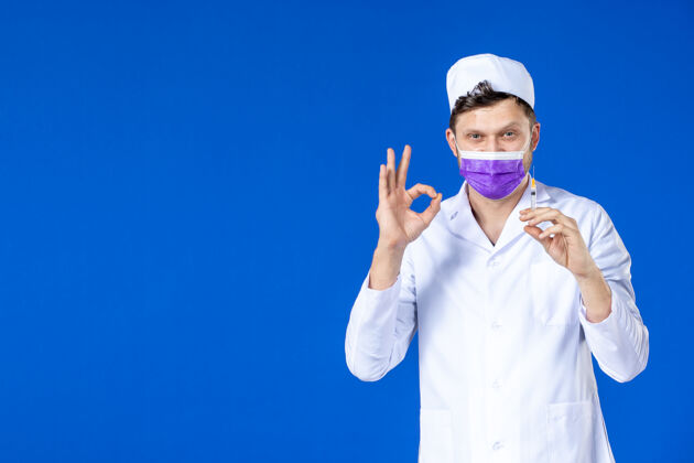 注射身穿医疗服 戴着紫色口罩的男医生正对着蓝色的脸拿着针剂男医生西装药品