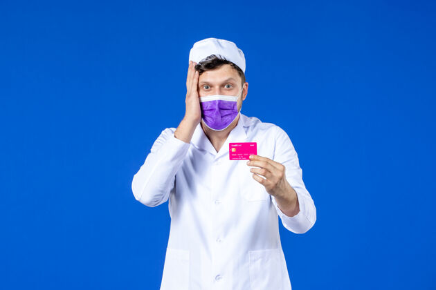 实验室外套前视图中的男医生穿着医疗服和面具持有信用卡的蓝色药品信用医院