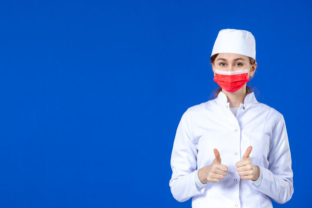 疾病身穿医疗服的年轻护士的正视图 蓝色的面具上有红色的面具制服套装医院