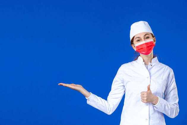 医院身穿医疗服的年轻护士的正视图 蓝色的面具上有红色的面具疾病病毒服装