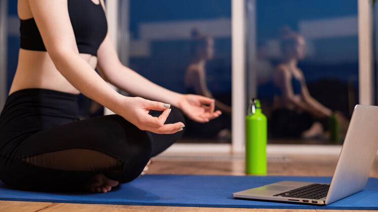 女人穿着运动服的年轻女子正坐在瑜伽垫上冥想 面前放着笔记本电脑健身坐着女孩