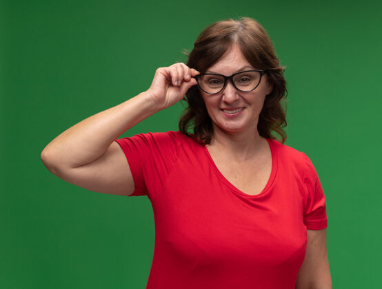 欢呼快乐的中年妇女穿着红色t恤 戴着眼镜 站在绿色的墙上 欢快地笑着中年站年龄