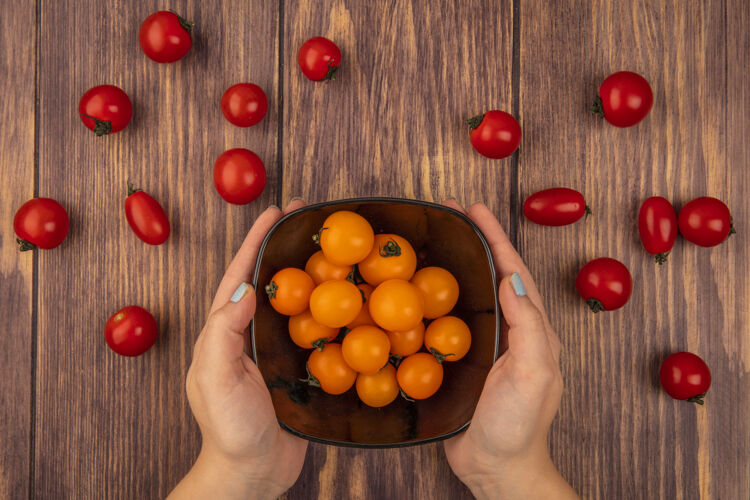 番茄顶视图女性手拿着一碗橙色的樱桃西红柿在木制表面持有有机樱桃