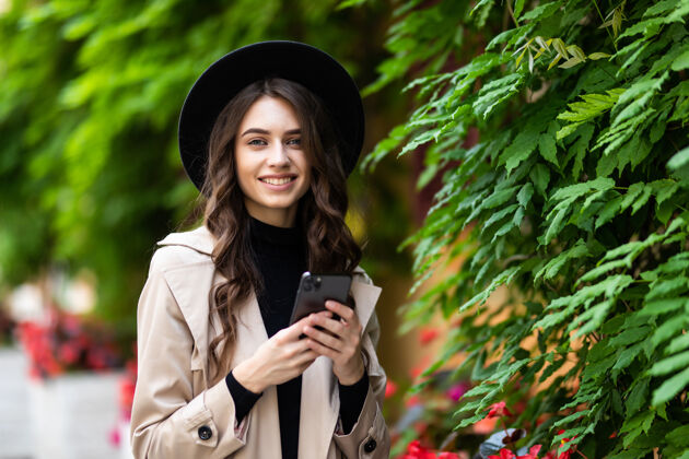 城市戴帽子的年轻女子在城市里散步 用的是智能手机散步的时髦人士用的是手机 为社交网络拍照女人周末用户