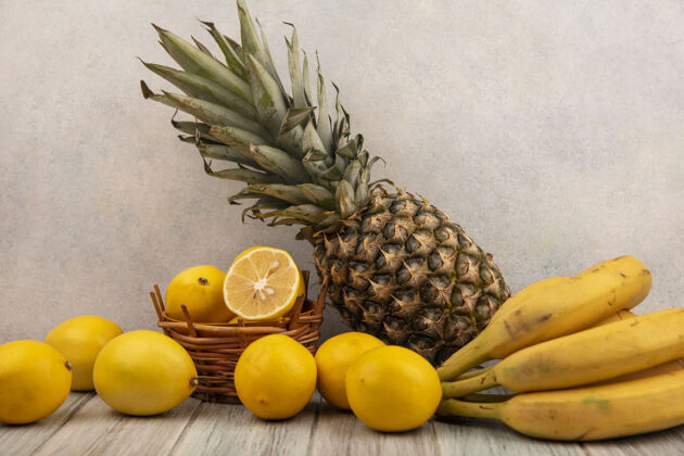 香蕉侧视图黄色柠檬桶柠檬香蕉和菠萝隔离在一个灰色的木桌上的白色表面柠檬厨房配料