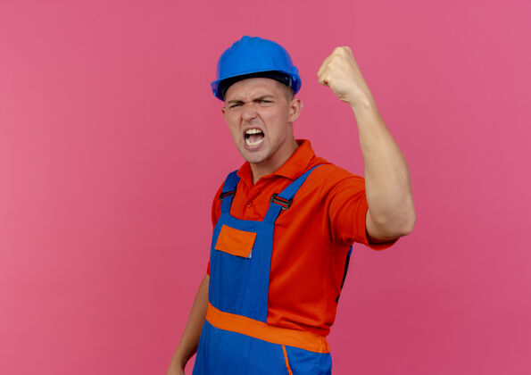 安全快乐的年轻男性建设者穿着制服 戴着安全帽做着坚强的手势强壮佩戴工人