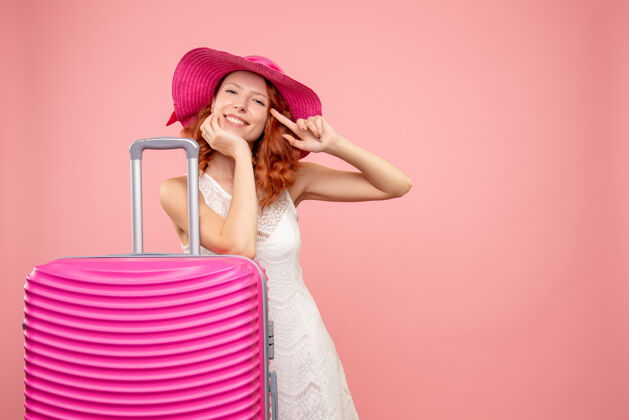 夏天年轻的女性游客与粉红色的帽子和粉红色的墙壁上的包的正面视图可爱头发前面