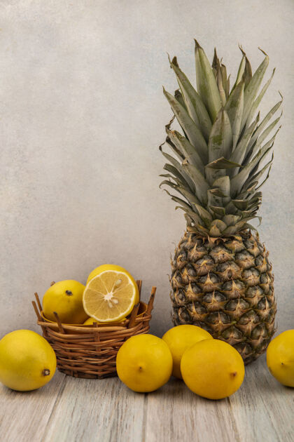 美味一桶新鲜柠檬的侧视图 柠檬和菠萝被隔离在白色表面的灰色木桌上营养壁板菠萝