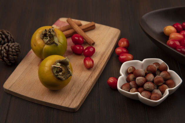 甜点木制厨房板上的柿子水果俯视图 肉桂棒和榛子放在一个碗上 木盆表面孤立着一个山茱萸樱桃营养新鲜配料