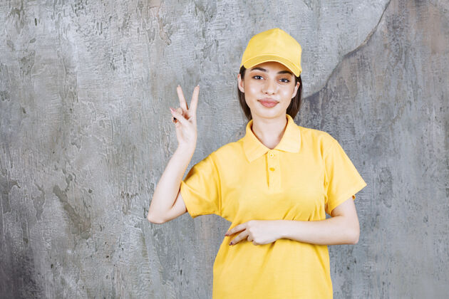 促销身着黄色制服的女服务人员站在水泥墙上 送上和平和平姿势成人