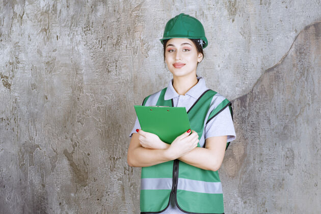 成人身着绿色制服 头戴安全帽的女工程师拿着项目文件夹建筑师人体模型雇员