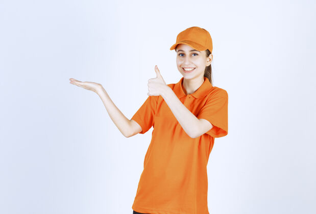 休闲女信使穿着橙色制服 戴着帽子 大拇指朝上运输好送货