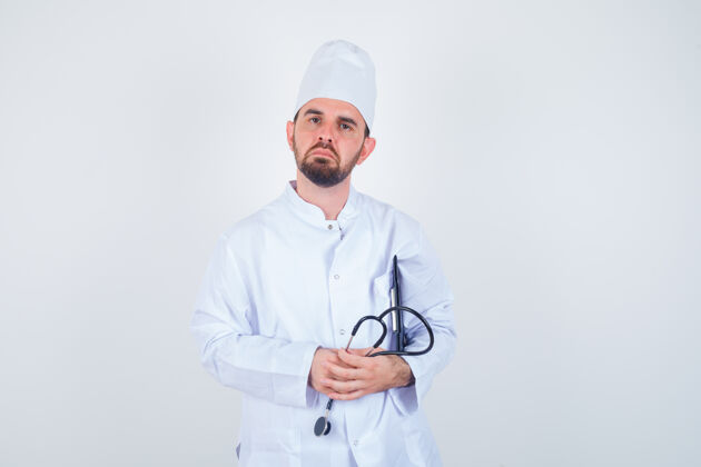 年轻年轻的男医生拿着剪贴板和听诊器 穿着白色制服 看上去很小心 正前方视图专业思维职业