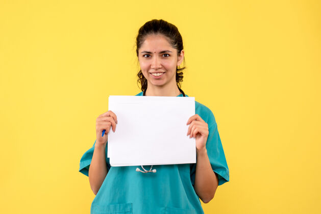背景正面图快乐美丽的女医生双手拿着黄色背景的文件微笑人防护服