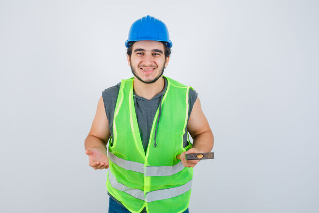 前面年轻的建筑工人拿着锤子 穿着工装 把手掌放在一边 看上去很高兴 正前方表情模特人
