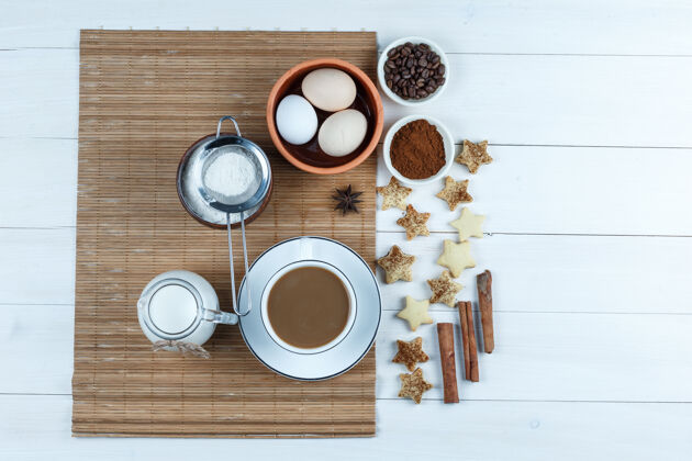 美食俯视图：鸡蛋 牛奶罐 咖啡杯 咖啡豆和面粉放在垫子上的面粉 星星饼干 白色木板背景上的肉桂水平酒吧食物肉桂