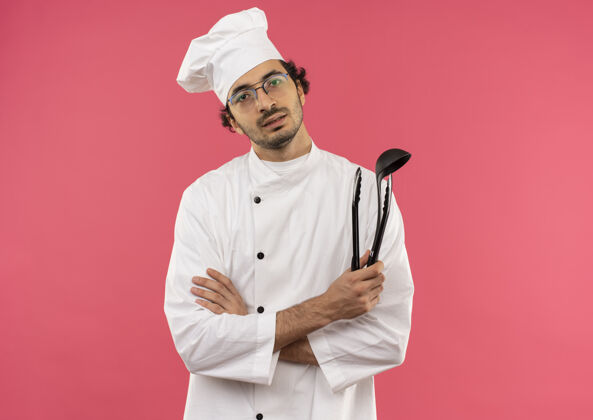 穿年轻的男厨师穿着厨师制服 戴着眼镜 手里拿着抹刀 双手交叉男年轻烹饪