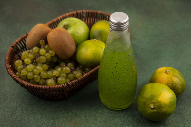 葡萄侧视图绿色的橘子与苹果猕猴桃和葡萄在一个篮子与一瓶果汁在绿色的墙上瓶子果汁苹果