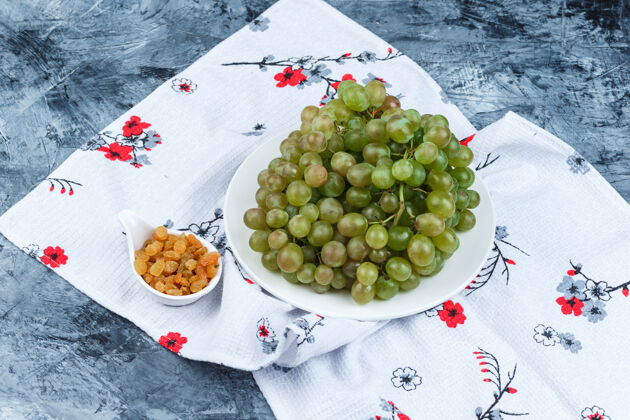 树枝绿色葡萄在一个白色的盘子里 葡萄干高角度的视角放在肮脏的石膏和厨房毛巾的背景上角毛巾多汁