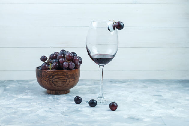 自然一杯葡萄酒和黑葡萄放在一个粘土碗里 背景是灰色和木质的侧视图葡萄藤健康有机
