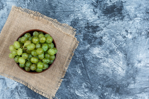大一碗白葡萄放在深蓝色大理石背景的垫子上 平铺着食物夏天葡萄酒